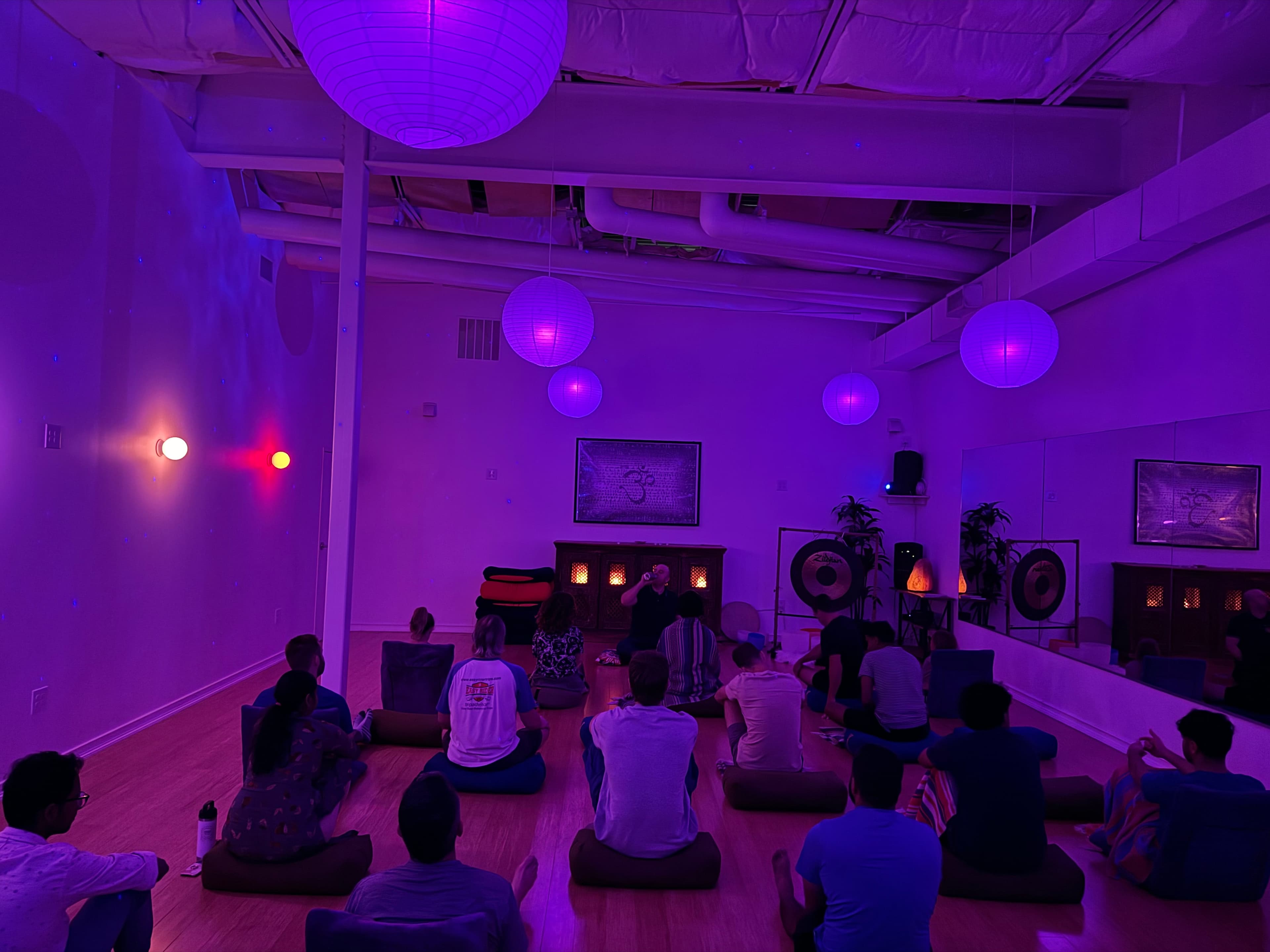 The Daily Sit — group meditation session in purple-lit room with lanterns and gongs